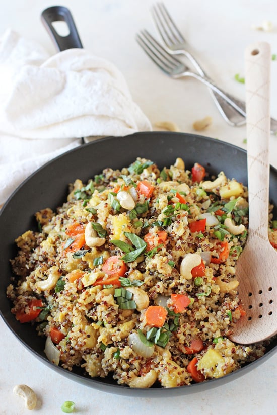 A black skillet filled with Pineapple Cashew Quinoa Fried Rice with a wooden spoon in the pan.