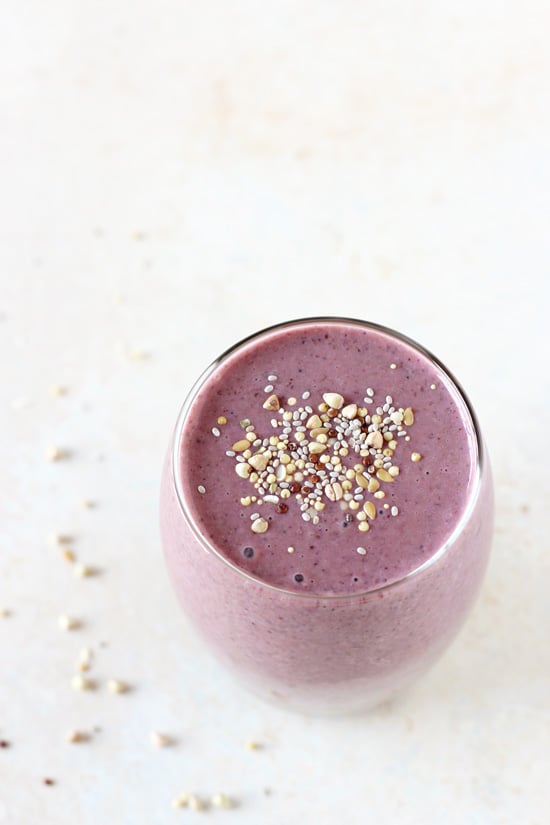 A glass filled with Berry Breakfast Smoothie with seeds scattered around.
