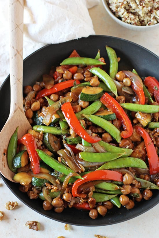 A black skillet filled with Bell Pepper, Snap Pea and Zucchini Stir-Fry with a wooden spoon in the pan.