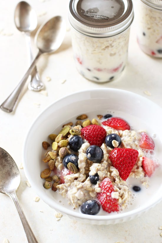 A white bowl filled with Berry Overnight Oats with pistachios and a spoon to the side.