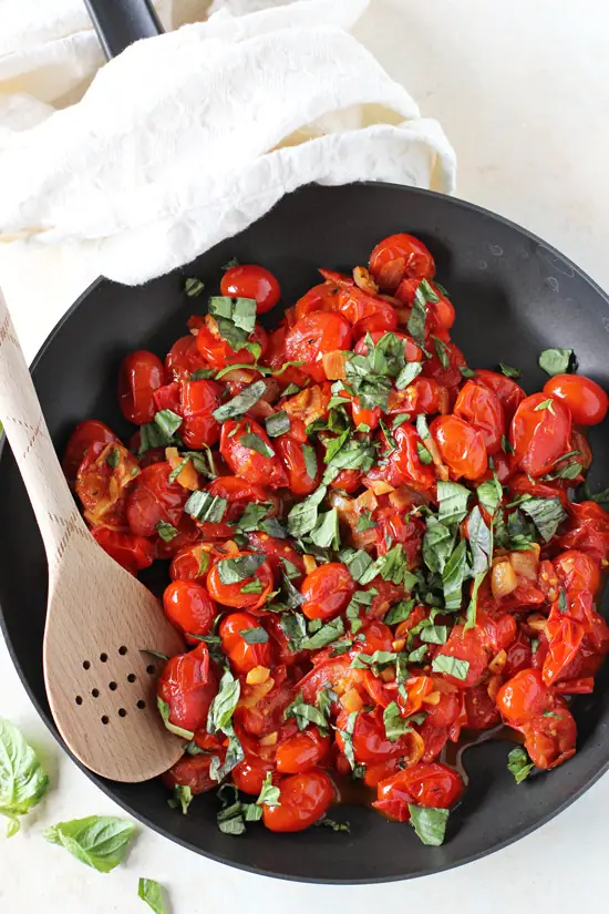 A black skillet filled with Fresh Cherry Tomato Sauce with a wooden spoon in the pan.