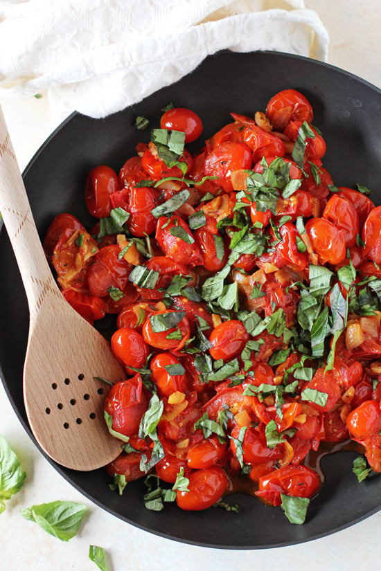 A black skillet filled with Cherry Tomato Pasta Sauce with a wooden spoon in the pan.