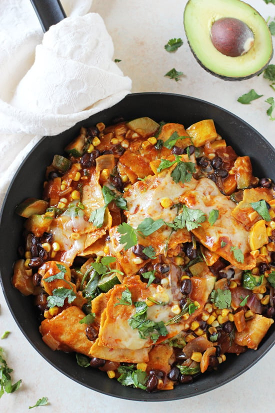 A black pan filled with Summer Vegetable Skillet Enchiladas with an avocado to the side.