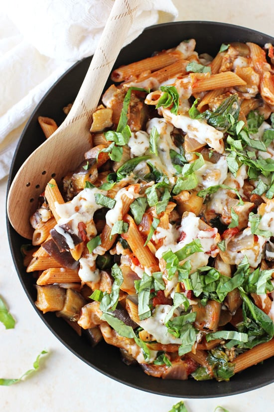 A black skillet filled with Healthy Eggplant Pasta with a wooden spoon in the pan.