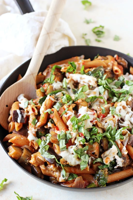 A black skillet filled with Eggplant Pasta with a wooden spoon in the dish.