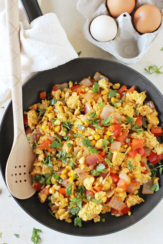 A black skillet filled with Mexican Scrambled Eggs with a carton of eggs in the background.