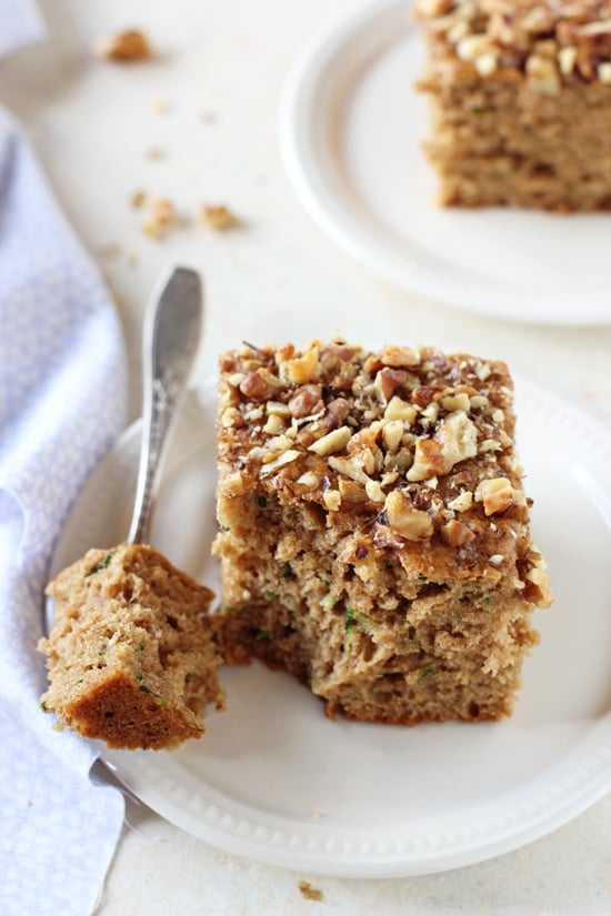 Two slices of Healthy Zucchini Bread on white plates with a fork and blue napkin to the side.