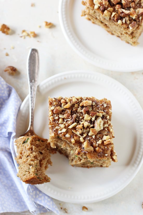 Two squares of Honey Cinnamon Zucchini Bread on white plates with a bite taken out with a fork.