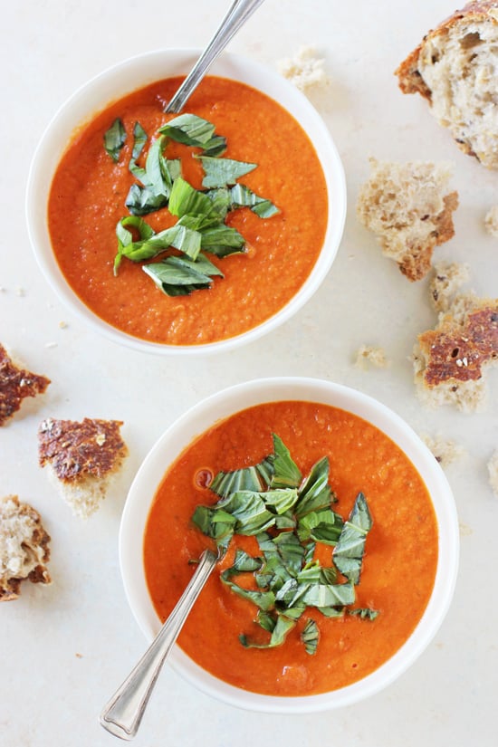 Two white bowls filled with Roasted Cherry Tomato Soup with torn bread to the side.