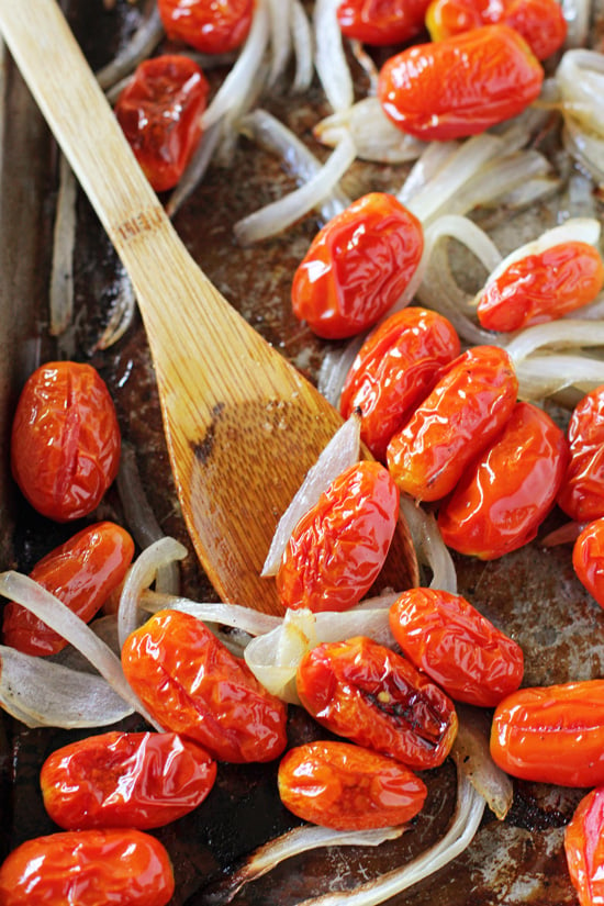 A baking sheet with roasted tomatoes, onions and a wooden spoon.