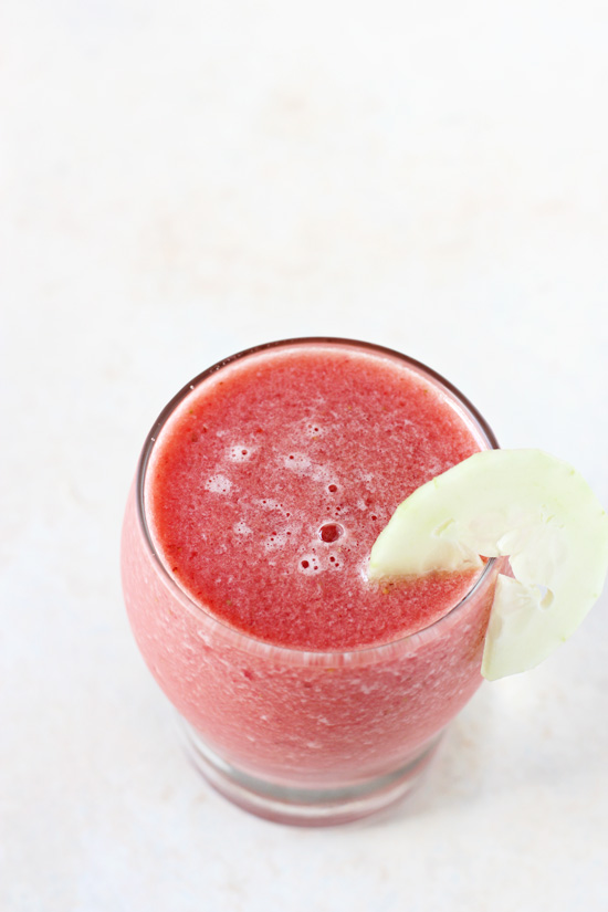 A glass filled with Watermelon Berry Smoothie with a sliced cucumber on the rim.