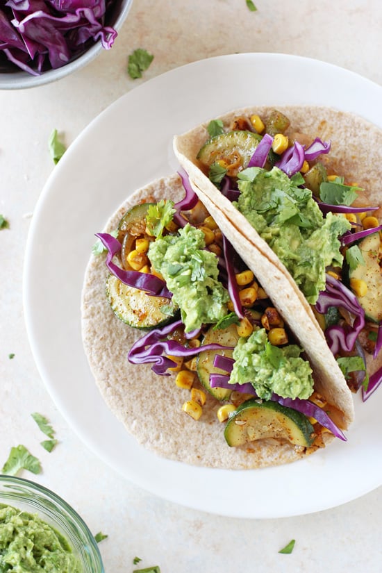Two Zucchini and Corn Tacos on a white plate with cabbage and guac to the side.