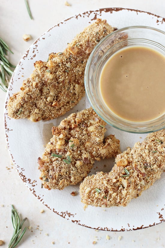 A white plate with several Baked Rosemary Walnut Chicken Tenders and a bowl of mustard dipping sauce.