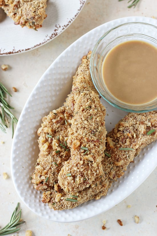 A white platter with Walnut Crusted Chicken Tenders and a bowl of dipping sauce.