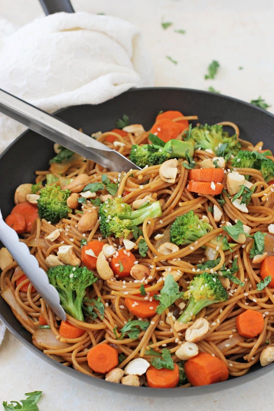 A black skillet filled with Broccoli Carrot Noodle Stir-Fry with tongs in the pan.