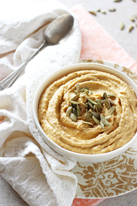 A white bowl filled with Sweet Potato Hummus with a white napkin and spoon to the side.