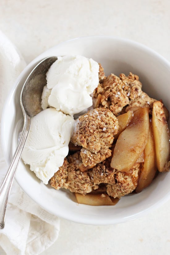 A white bowl filled with Vegan Apple Cobbler and topped with vanilla ice cream.