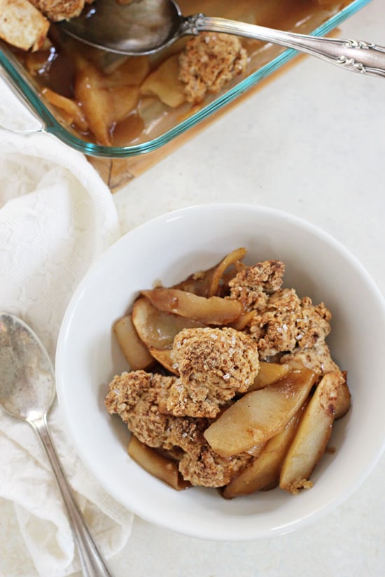 A white bowl filled with Vegan Apple Cobbler and a baking dish in the background.