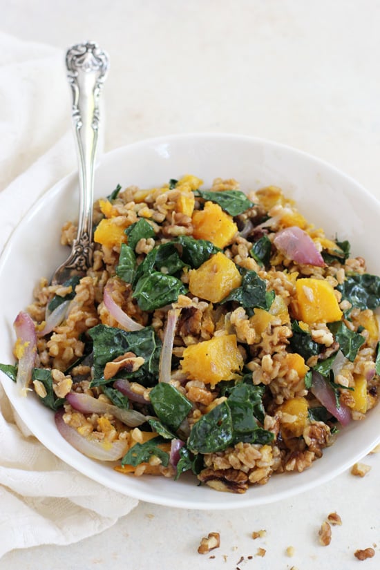 A white bowl filled with Fall Farro Salad and a silver serving spoon.