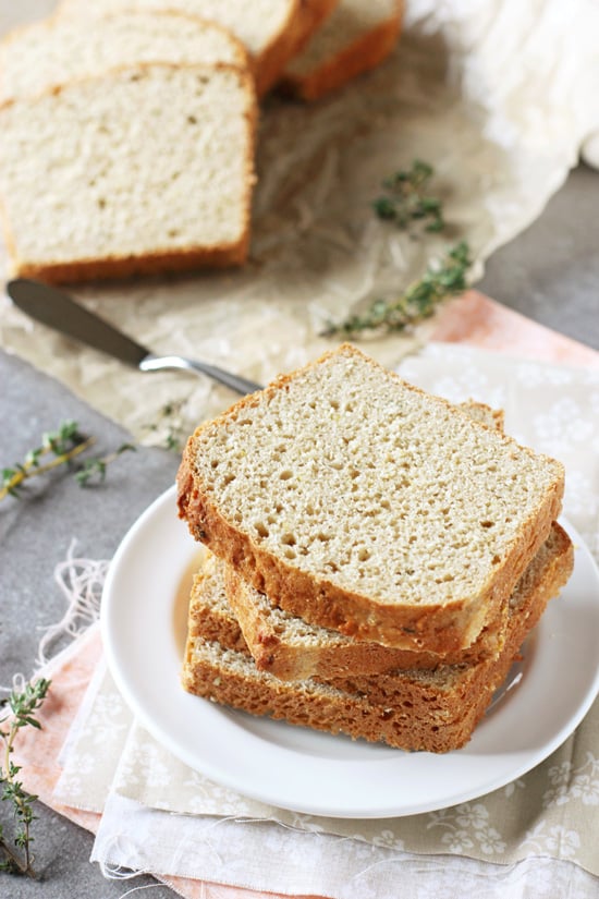 Three slices of Lemon Thyme English Muffin Bread stacked on a white plate with more slices in the background.