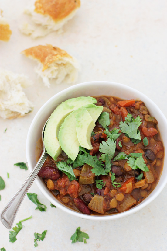 A white bowl filled with Vegetarian Pumpkin Chili topped with sliced avocado and cilantro.