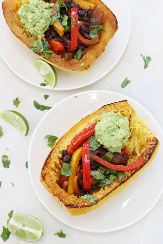 Two stuffed Mexican Spaghetti Squash on white plates with lime slices.