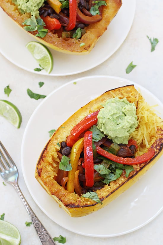 Overhead view of two stuffed Mexican Spaghetti Squash on white plates with a fork to the side.