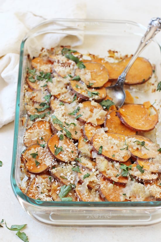 Healthier Sweet Potato Gratin in a glass baking dish with a silver serving spoon.