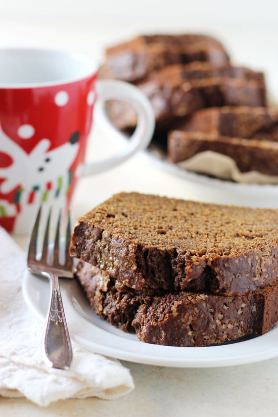Two pieces of Healthy Maple Gingerbread Loaf on a plate with a cup of coffee in the background.