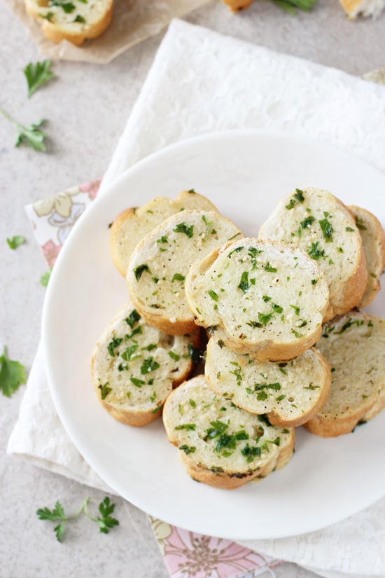 Overhead view of slices of Freezer Garlic Bread stacked on a white plate.