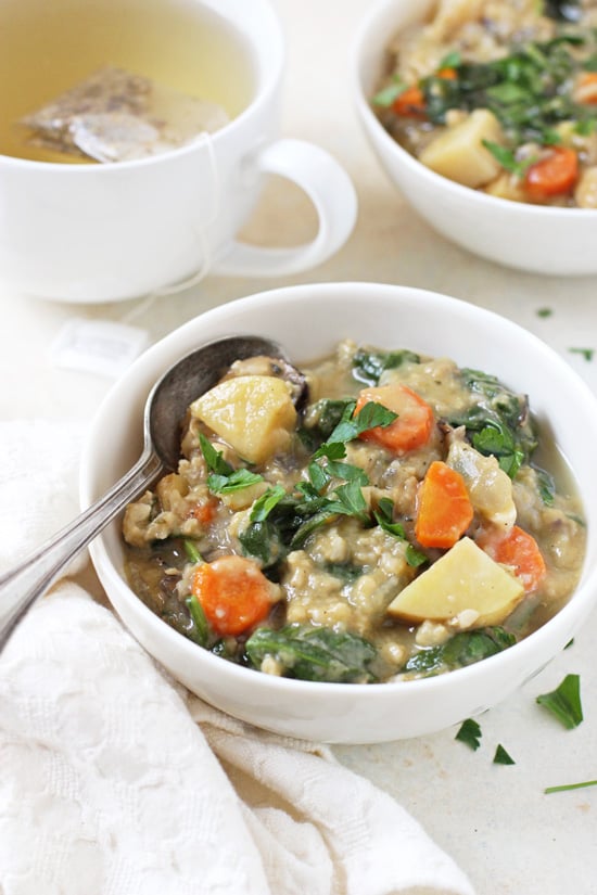 Side angle view of a bowl of Slow Cooker Creamy Veggie & Wild Rice Soup with a cup of tea and another bowl of soup in the background.