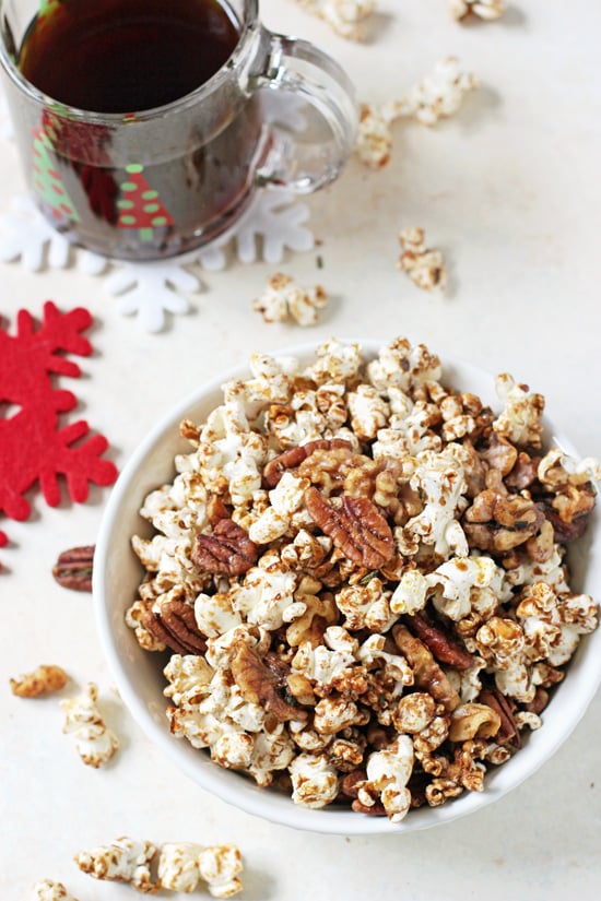A bowl filled with Popcorn Snack Mix with a cup of coffee in the background.