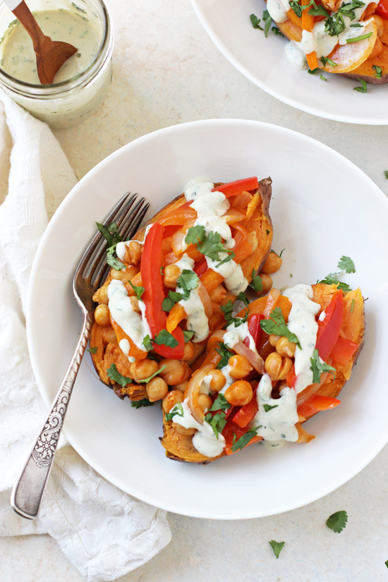 A Buffalo Chickpea Stuffed Sweet Potato in a white bowl with a fork and a jar of tahini ranch to the side.