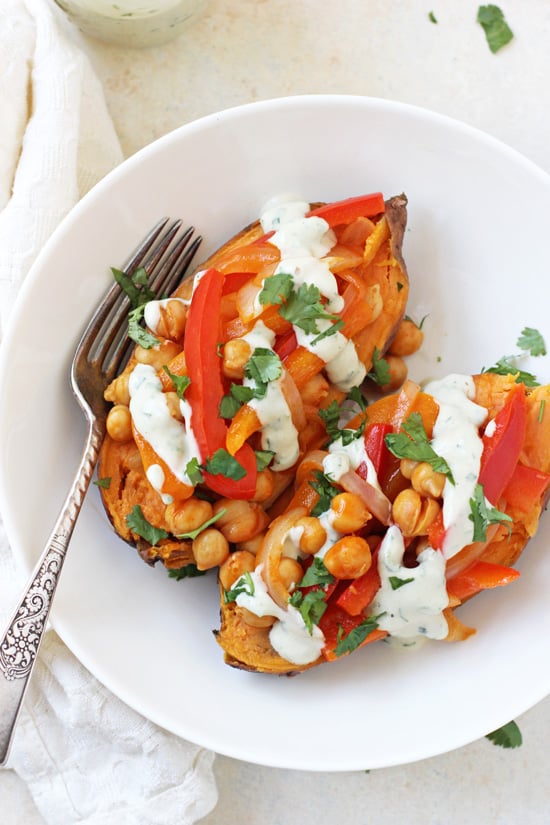 Overhead view of a Buffalo Chickpea Stuffed Sweet Potato in a bowl with a fork and drizzled with tahini ranch.