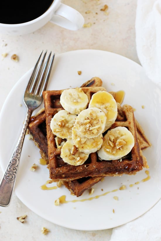 A white plate with two Healthy Banana Walnut Waffles topped with sliced banana and a fork on the plate.