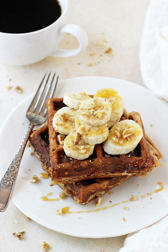 Side angle view of two Healthy Banana Waffles with a fork on the plate and a cup of coffee in the background.