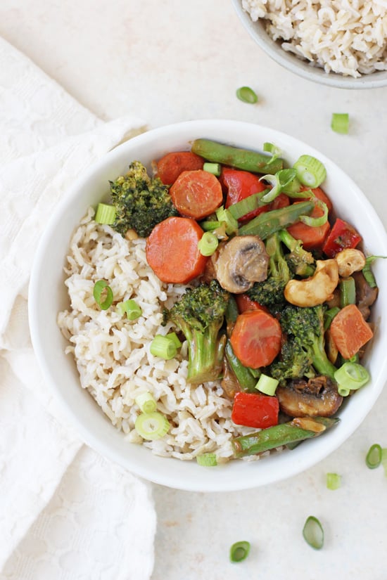 A bowl of Peanut Ginger Vegetable Stir-Fry with brown rice and a white napkin to the side.