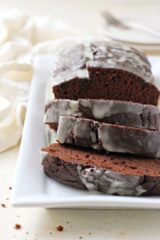 A loaf of Chocolate Sweet Potato Bread on a white platter with three slices cut out.