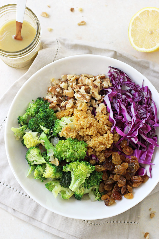 Overhead view of Crunchy Broccoli Quinoa Salad in a bowl with dressing and a lemon to the side.