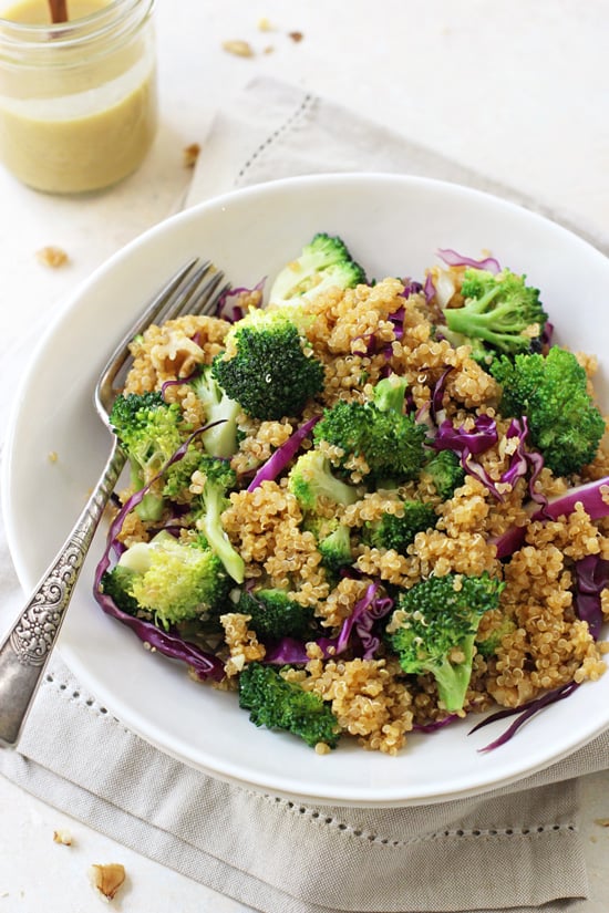 Side angle view of Broccoli Quinoa Salad in a bowl with a fork and a jar of dressing in the background.