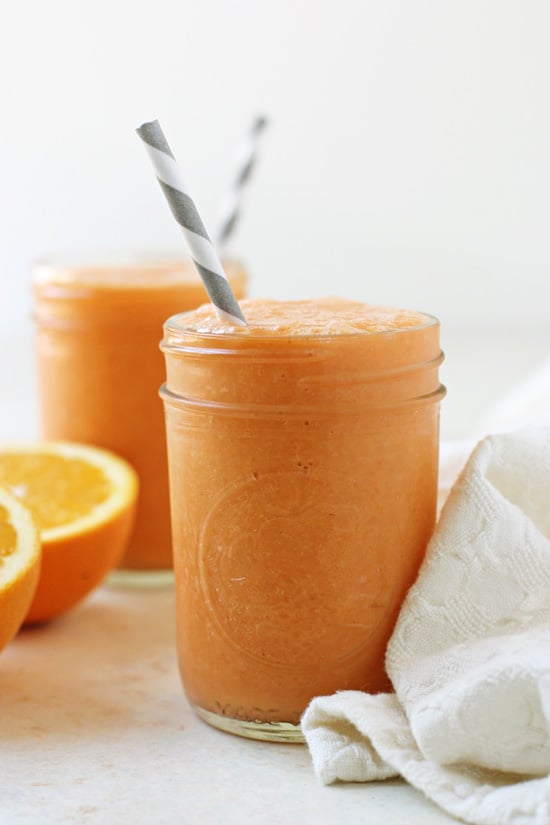 Side angle view of Orange Carrot Smoothie in two glass jars with a white napkin to the side.