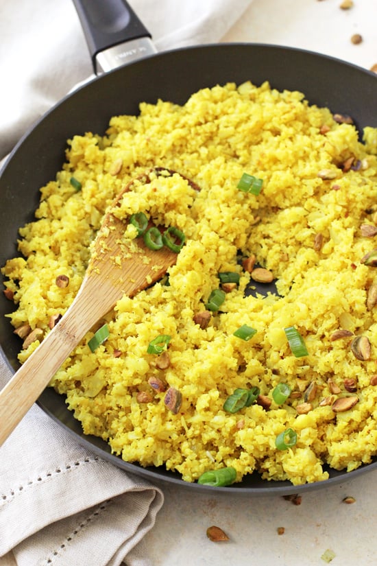 Turmeric Cauliflower Rice in a black skillet with a wooden spoon in the pan.