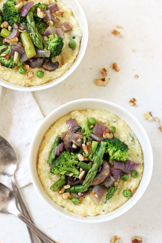 An overhead view of two white bowls filled with Spring Polenta Primavera and two spoons on the side.