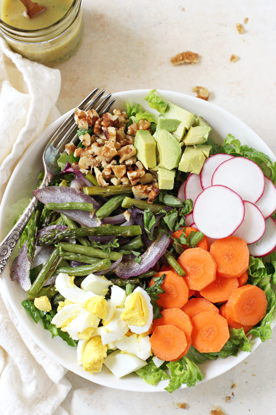 An overhead view of a bowl filled with Spring Vegetable Cobb Salad and a jar of dressing to the side.