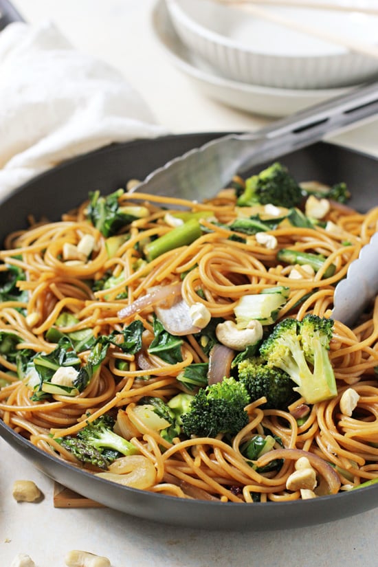 Side angle view of Spring Vegetable Lo Mein in a skillet with tongs.