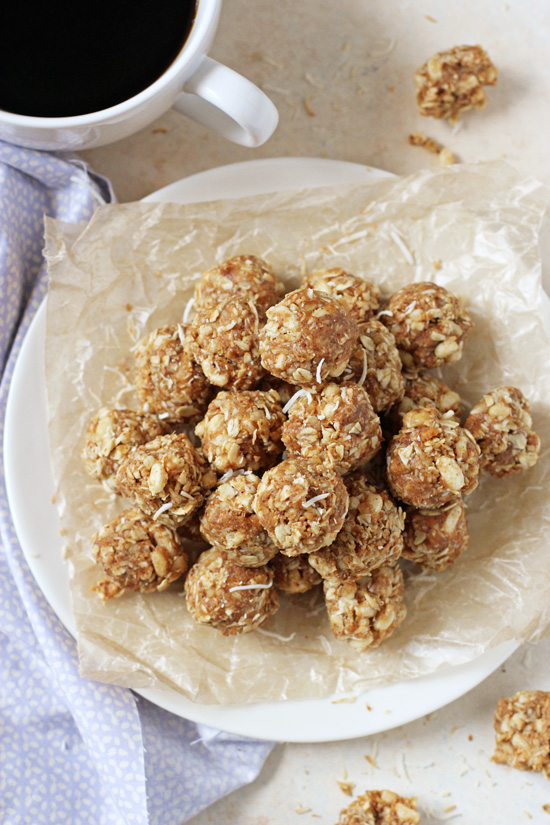 A plate stacked with Toasted Coconut and Macadamia Energy Bites with a cup of coffee and more bites to the side.