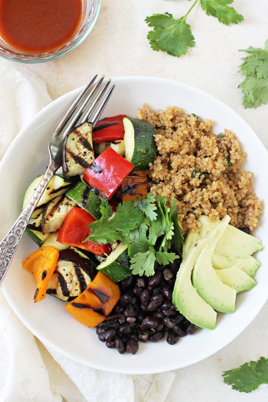 A Grilled Vegetable Enchilada Bowl with a fork and a napkin plus enchilada sauce to the side.