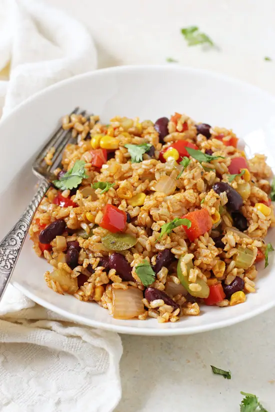 Vegetable Cajun Brown Rice in a white bowl with a fork and a napkin to the side.