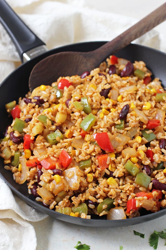 Side angle view of Vegetable Cajun Brown Rice in a skillet with a wooden spoon.