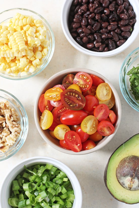 Small bowls filled with cherry tomatoes, black beans, corn kernels, walnuts and green onion.